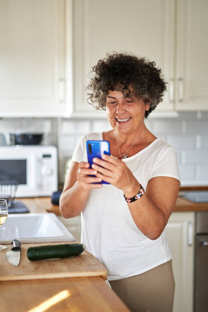 istock Mature woman using phone in kitchen 1458838233