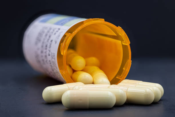 Closeup image of medical drugs spilling out of orange prescription bottle on black background White pills with orange bottle. Pills spilling out of orange bottle. Blurry prescription tag is visible on the bottle. Foreground pills are in sharp focus, the rest of pills and bottle are blurry. Black natural background. Extremely sharp stock photo. Pill jar is open, cap is not visible on the image. antibiotic stock pictures, royalty-free photos & images