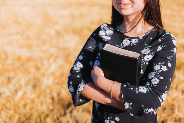 Young smiling christian teenage woman holding a bible under her arm in the field. Sola scriptura. Copy space Young smiling christian teenage woman holding a bible under her arm in the field. Sola scriptura. Copy space mormon woman photos stock pictures, royalty-free photos & images