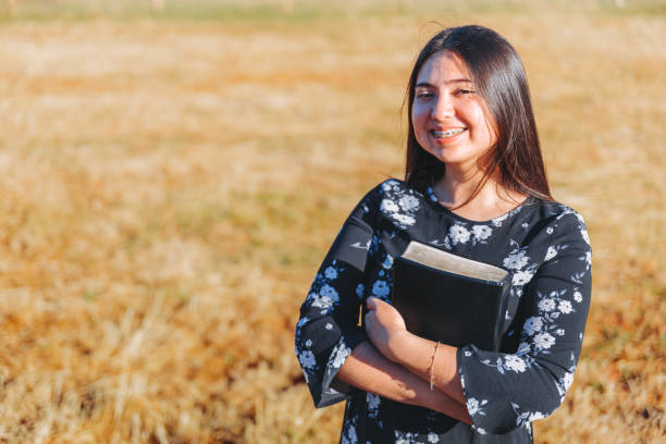 Young smiling christian teenage woman holding a bible under her arm in the field. Sola scriptura. Copy space Young smiling christian teenage woman holding a bible under her arm in the field. Sola scriptura. Copy space mormon woman photos stock pictures, royalty-free photos & images