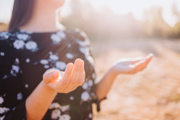 Religious believer woman praying, raising hands to to receive God's spirit Religious believer woman praying, raising hands to to receive God's spirit, in the field at sunset. Faithful person praying to heaven for God's blessings chilean dress pictures stock pictures, royalty-free photos & images