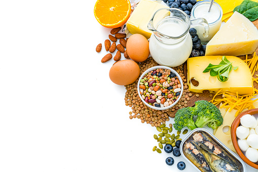 High angle view of a group of food with high calcium content arranged at the right of a white background leaving copy space at the left. The composition includes dairy products souch milk, yogurt, butter, various cheeses, mozzarella cheese, eggs, sliced orange, broccoli, mixed beans, sardines, almonds among others. High resolution 42Mp studio digital capture taken with SONY A7rII and Zeiss Batis 40mm F2.0 CF lens
