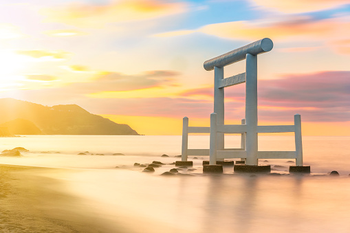 kyushu, japan - dec 07 2022: Sunset long exposure photography of a Japanese white wooden torii arch with its pillars in the sea along the Itoshima Beach of Fukuoka famous for Couple Rocks called Sakurai Futamigaura's Meoto Iwa.