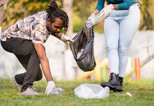 Two diverse young volunteers picking up plastic litter together in a public park during a community clean-up project