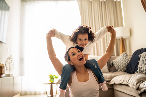 Mother playing piggyback with her daughter in the living room at home