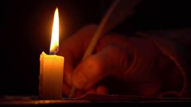 A hand writing in a quill pen by a candle