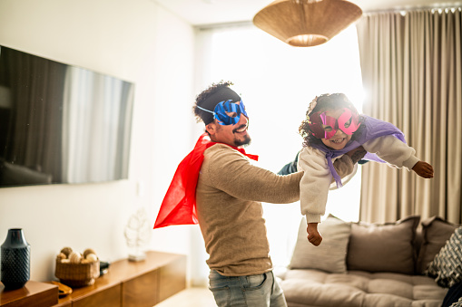 Father and daughter playing superhero in the living room at home