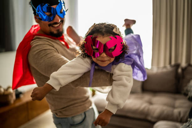 retrato de padre e hija jugando a superhéroes en la sala de estar de su casa - disfrazar fotografías e imágenes de stock