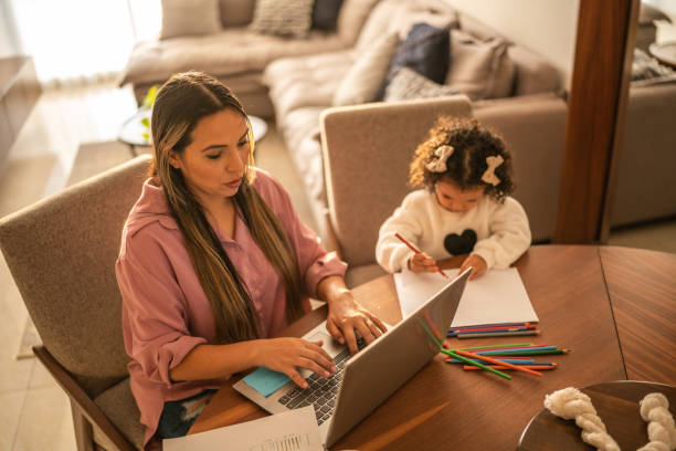 istock Young woman working while her daughter draws beside her at home 1458849770