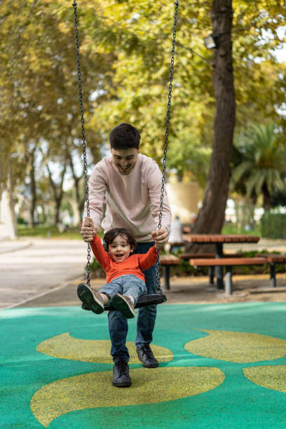 istock Father playing with his son on the swing in the park 1458852073