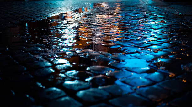 pfütze zwischen kopfsteinpflaster in der nacht mit reflektiertem licht in rom, italien. - blue rain rome italy stock-fotos und bilder