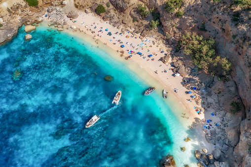 Top view of seascape with beautiful coastline and small sandy beach with colorful umbrellas. Sea coast with blue, turquoise clear water on a sunny day, aerial drone shot