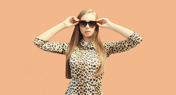Portrait of beautiful blonde young woman wearing leopard dress and sunglasses on background