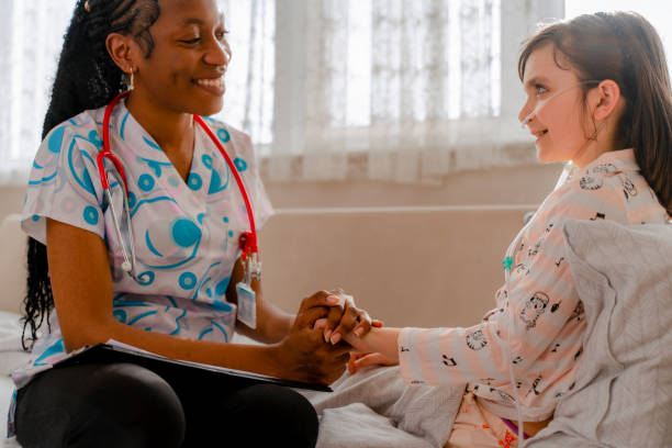 young home health nurse and the little girl with cancer embrace and laugh together.