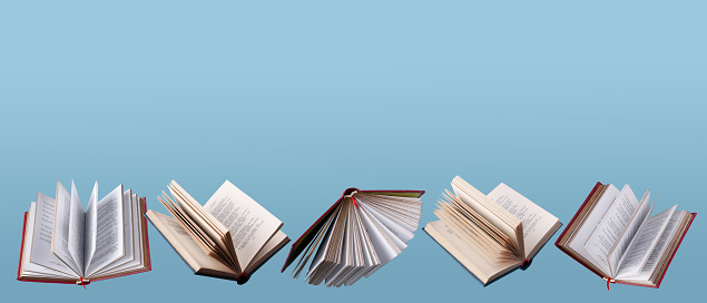 Stack of books on a wooden library shelf, the one on top open , multicolored book spines in a row in the background. Copy space on the left.