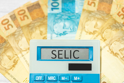 The initials SELIC referring to the basic interest rate in Brazil written on the display of a calculator with Brazilian Real banknotes in the composition. Brazilian economy and investments.