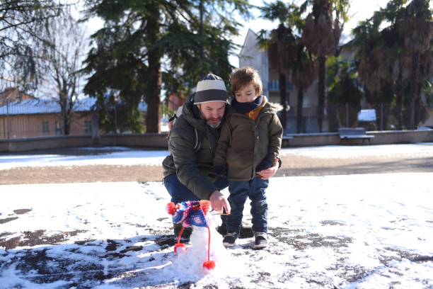 A photo of a grandfather and grandson playing in the snow. They have winter clothing. The grandfather is carrying the kid on back..