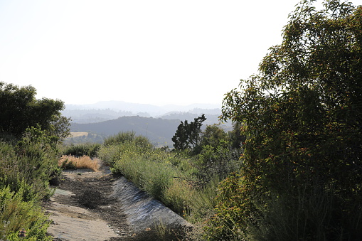 Panoramic views of a mountain trail featuring rich green scrub and light sandy clay with blue skys