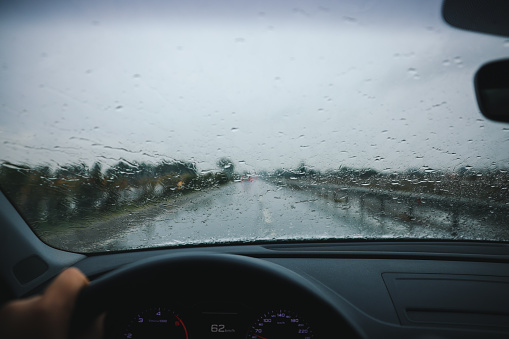 A car driving through a rainy highway with the windshield wipers in motion.