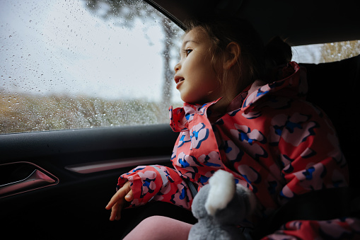 Little girl is looking trough the car window in rainy day