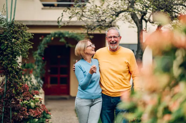 Portrait of a senior married couple holding keys and standing outside their new home on a moving day and hugging. Mature people outside their new house. Copy space. Investing in property.