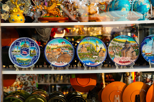 Various colorful hand-painted ceramic plates depicting tourist attractions on showcase of Georgian gift shop