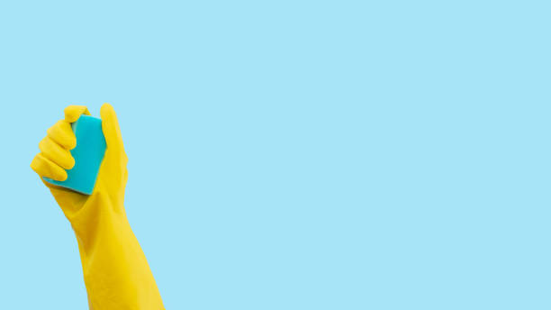 istock Blue sponge in yellow rubber glove on blue background. Minimal creative cleaning service concept. 1458891556