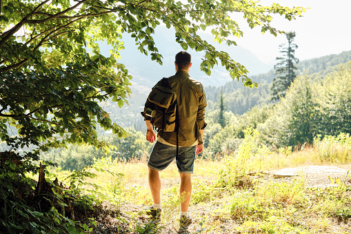 A man traveler walks through the woods. Beautiful wild nature landscape in forest. Hiking journey on tourist trail. Outdoor adventure. Travel and exploration. Healthy lifestyle, leisure activities