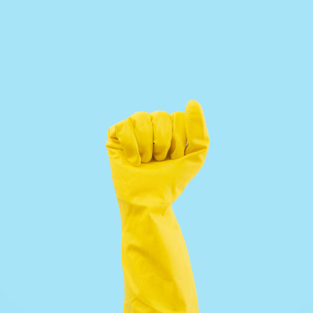 istock Hand in yellow rubber glove on blue background. Protective latex gloves. Minimal creative cleaning service concept. 1458891907