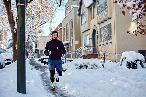 Male runner jogging on snow while exercising outdoors during winter.