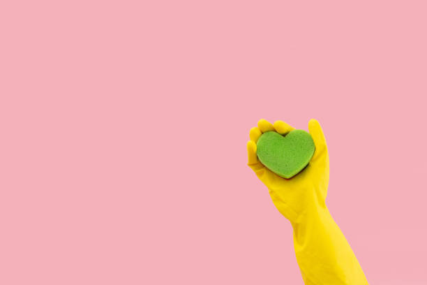 istock Heart shape green sponge and yellow rubber gloves on pink background. Minimal creative cleaning service concept. 1458892013