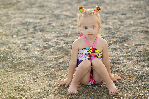 Little girl with Down syndrome sits on the summer coast