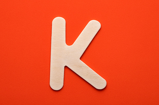 Alphabet letter K - White wood piece on orange foamy background