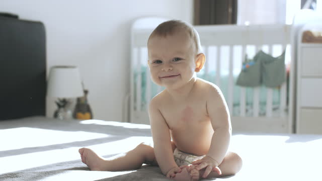 Charming baby boy sitting on bed at home.