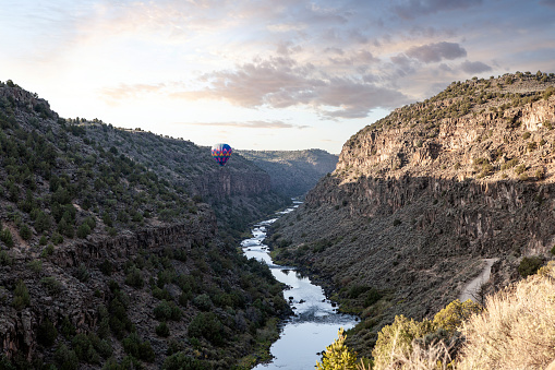 A colorful hot air balloon floating inside the Rio Grande Gorge in Arroyo Hondo, Taos County, New Mexico at sunrise.