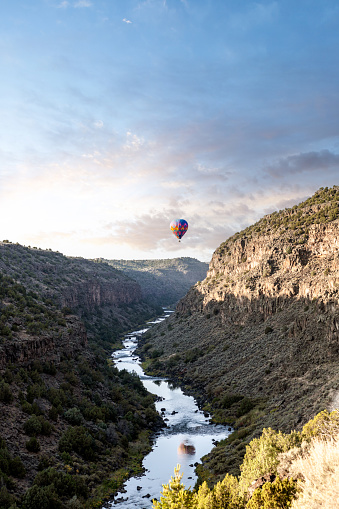 A colorful hot air balloon floating above the Rio Grande Gorge in Arroyo Hondo, Taos County, New Mexico at sunrise.