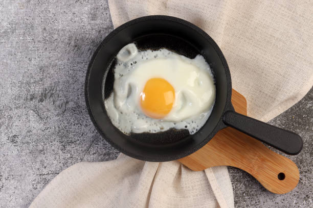 istock Sunny-Side Up Fried Eggs on a Cast-iron pan on a small cutting board on a dark grey background. Top view, flat lay 1458942767