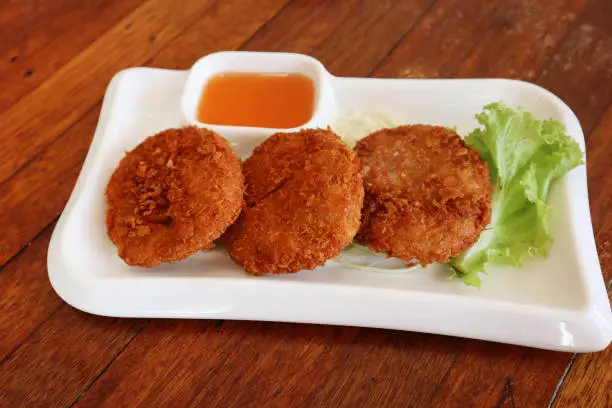 Photo of Thai-Style Deep-Fried Shrimp Cakes Recipe (Tod Man Goong) with sweet chili sauce and fresh lettuce on white plate.