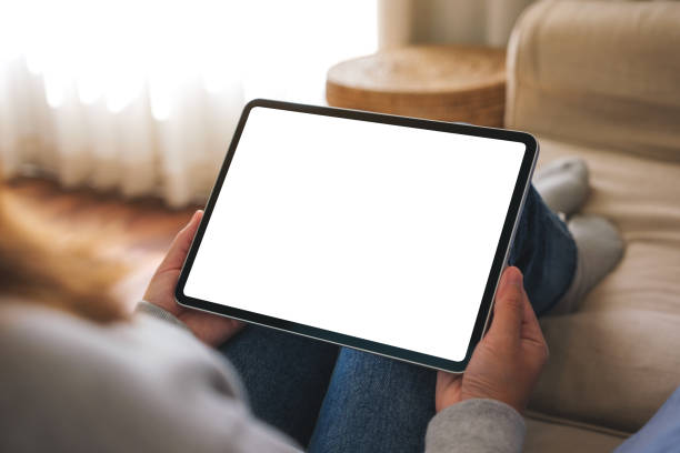 istock Mockup image of a woman holding digital tablet with blank desktop screen while lying on a sofa at home 1458955158