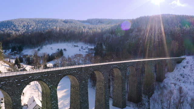 Train driving over a stone railway viaduct over a winter countryside.