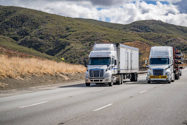 istock Two white big rigs semi trucks with different loaded semi trailers climbing uphill on the mountain road in California 1458966501
