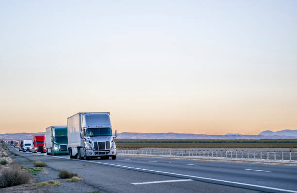 Professional long haul big rigs semi truck transporting cargo in semi trailers running on the straight highway road at twilight stock photo