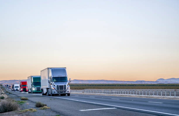 professional long haul big rigs semi truck transporting cargo in semi trailers running on the straight highway road at twilight - convoy imagens e fotografias de stock