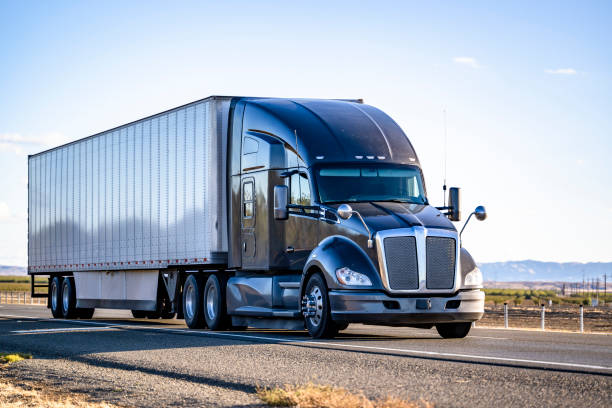 istock Black stylish big rig semi truck with truck driver sleeping compartment transporting cargo in dry van semi trailer driving on the flat highway road 1458968340