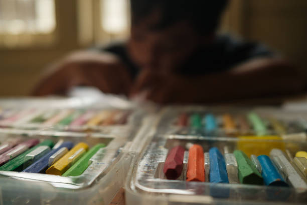 selective focus of lined crayons owned by an asian boy while he is drawing using his crayons and pencils on the table, Science, Technology, Education, Mathematics or STEM concept
