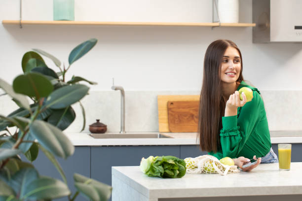istock An attractive brunette holds a green apple and smiles while standing at the kitchen table. 1458977120