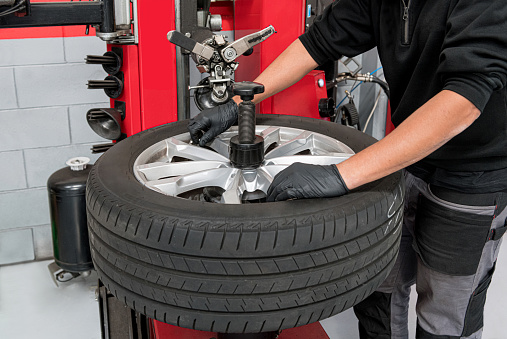 High angle of anonymous male technician in casual clothes and gloves turning screws on disc while dismantling tire during work in garage