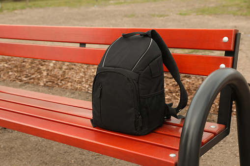 Stylish black backpack for camera on wooden bench outdoors