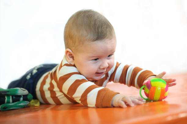 Baby plays with toys. Close-up view of cute baby boy lies on its stomach and play with toy. Playground for babies