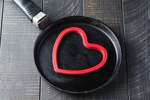 Cast-iron pan and heart shaped red silicone baking mold for baking pancakes to romantic breakfast. Valentine's Day concept. Dark wood background. Love and hearts theme